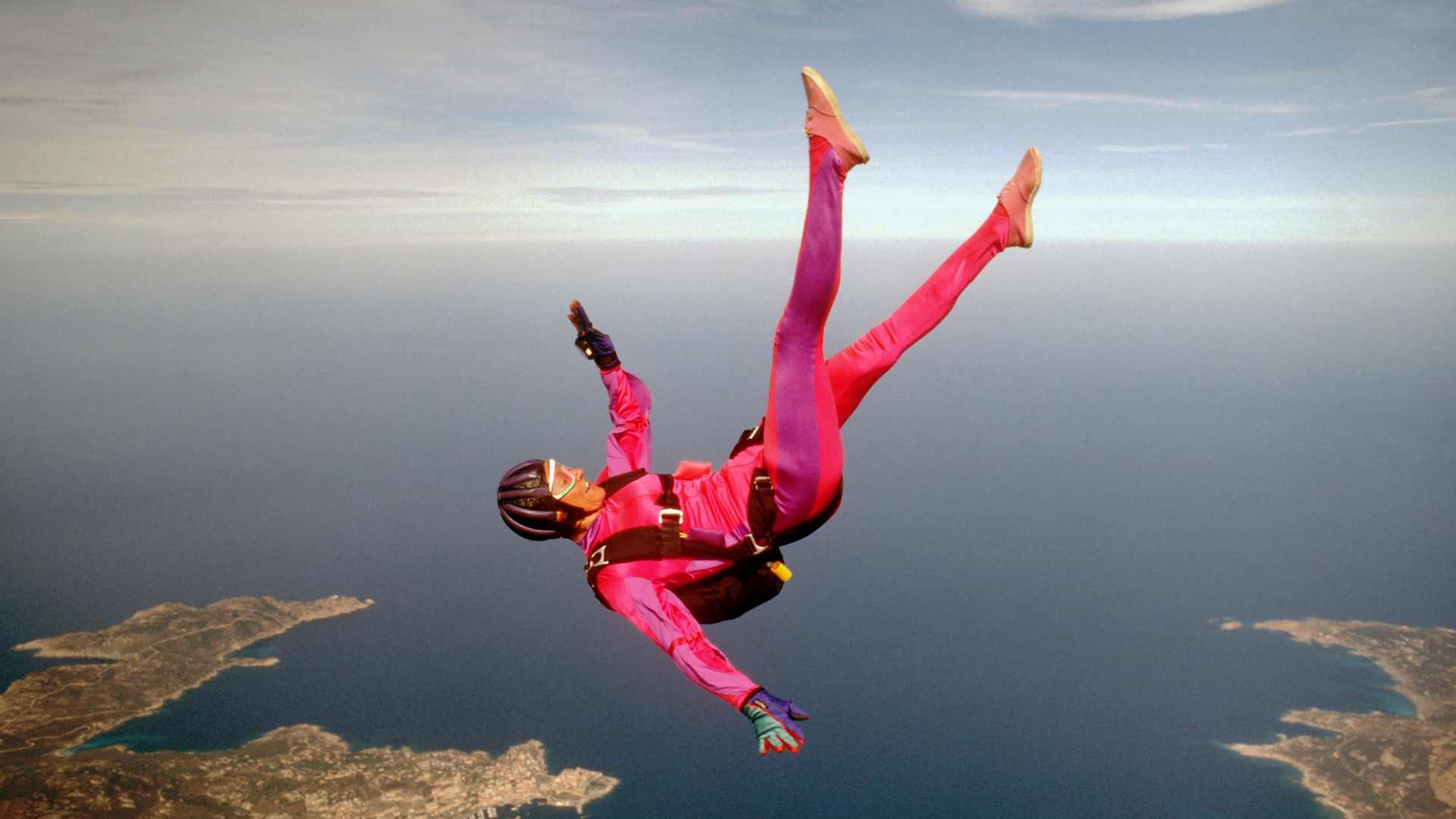 ExtremFallschirmsprung mit pinker Ausrüstung über einer Küstenlandschaft, vermittelt Mut, Innovation und Abenteuergeist.