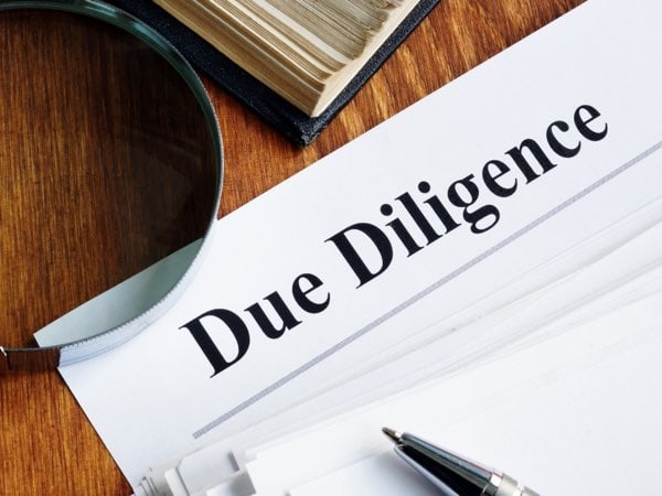 Due Diligence Dokument auf Papier mit Lupe und Stift für professionelle Geschäftsprüfung.