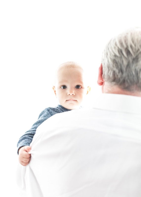 Entwicklungsförderung bei Babys, liebevolle Großeltern, Familienbindung, kinderfreundliche Atmosphäre, gemeinsame Zeit, Baby im Arme des Großvaters, Familienmomente, Eltern-Kind-Bindung, fürsorgliche Großeltern, Kindersicherheit.