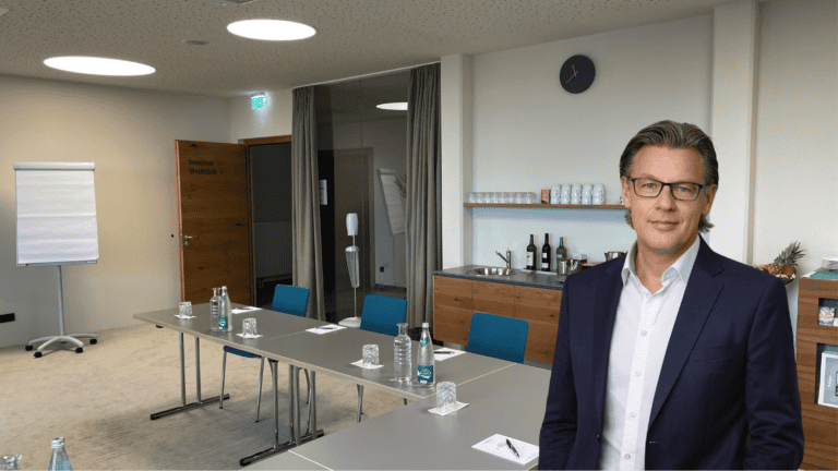 Heller, moderner Seminarraum mit Tisch, Stühlen, Whiteboard und Verpflegungsbereich, ideal für Workshops und Firmenveranstaltungen bei Slamanig Consulting & Training.